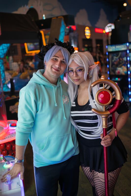 Cosplay couple posing together in an arcade, one holding a staff