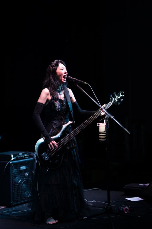 Vocalist and bassist on a dark stage, mid-note