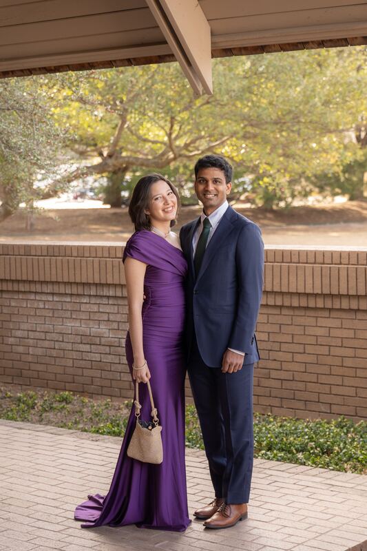 Couple in a purple gown and navy suit posing by a brick wall