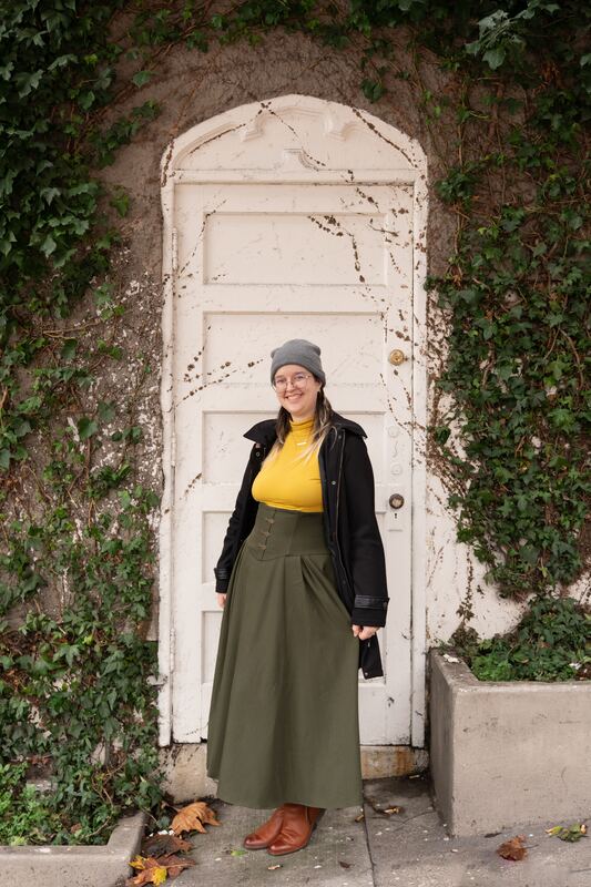 Woman in a green skirt at an ivy-covered white door